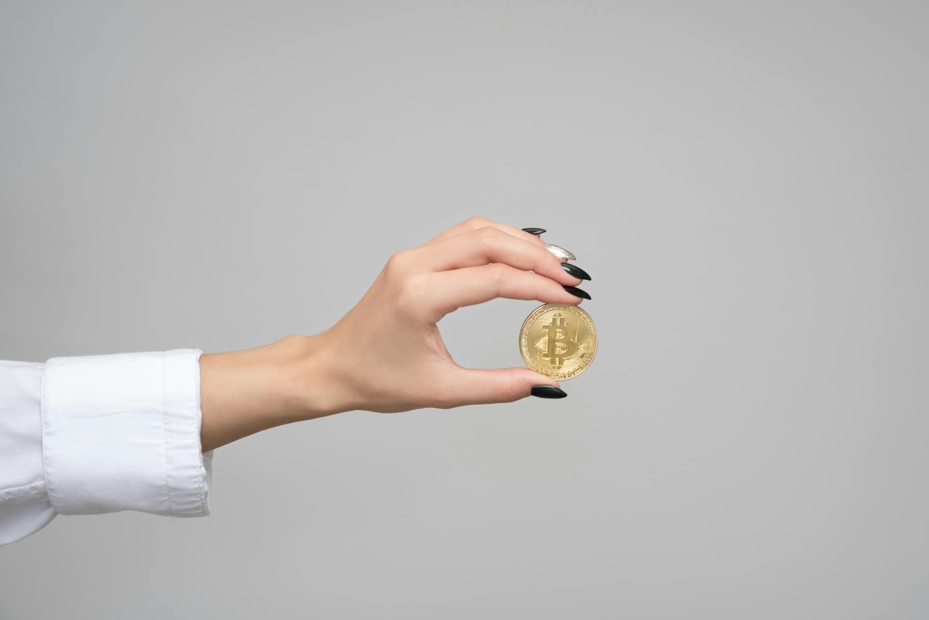 Close-up of a woman's hand holding a bitcoin coin against a neutral background.